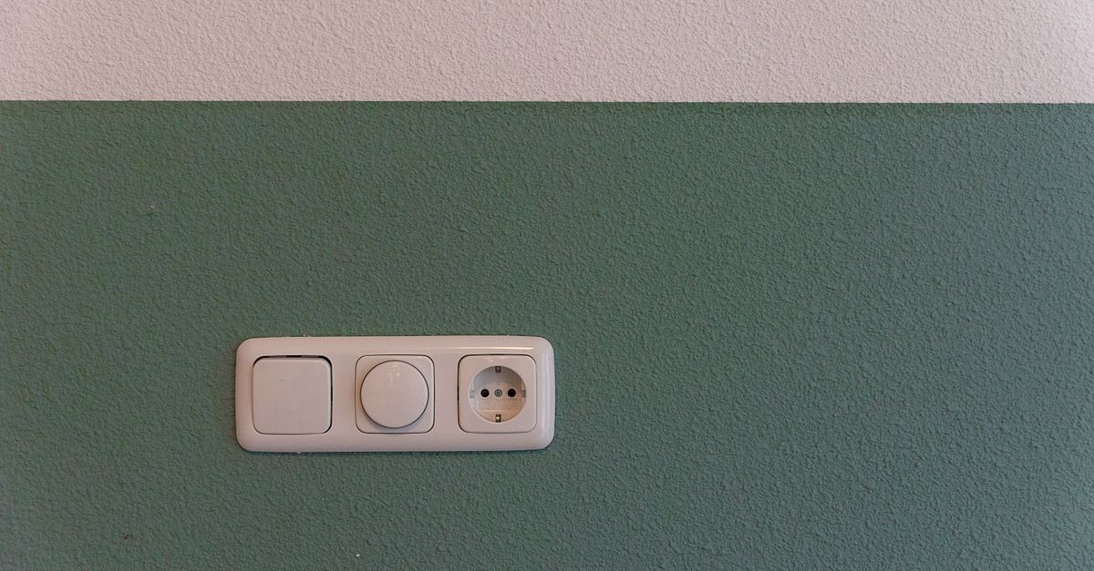 Close-up of a power outlet and switch on a textured green wall indoors.